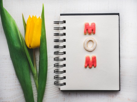 Beautiful greeting card with the word MOM. Blank page, bright tulip and glazed cookies on a white, isolated background. Top view, close-up, nobody. Congratulations for loved ones, relatives, familyの写真素材