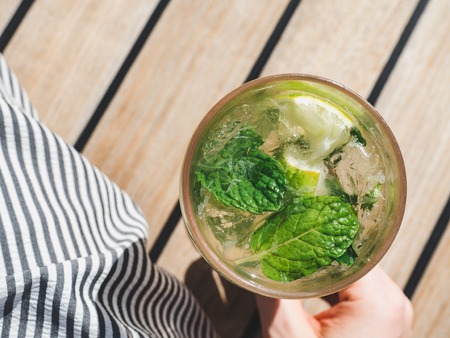 Beautiful glass with refreshing mojito and ice cubes on the background of the plank deck. Top view, close-up. Concept of leisure and travelの写真素材