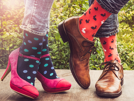Men's and women's legs in fashionable shoes, bright, multi-colored socks on a wooden terrace on the background of green trees and sunny rays. Close-up. Concept of Style, Fashion and Beautyの写真素材
