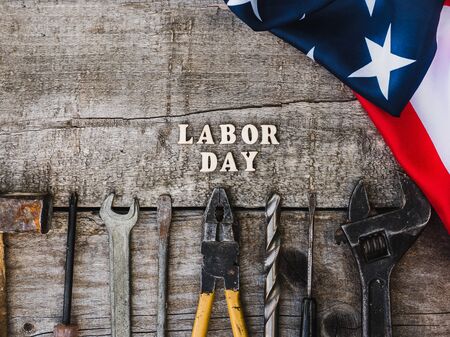 LABOR DAY. Hand tools, American Flag and wooden letters lying on the desk. Top view, close-up....