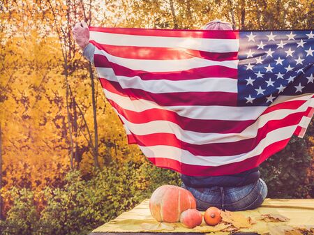 Attractive guy holding a US flag against the background of yellow trees and the setting sun. National holiday conceptの写真素材