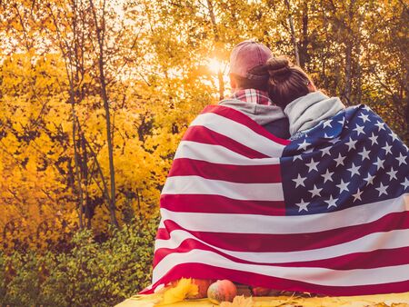 Happy married couple holding the US flag against the background of yellow trees and the setting sun. Happy relationship conceptの写真素材