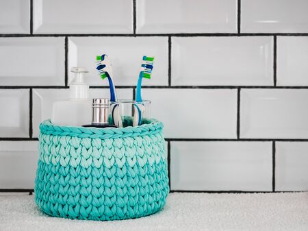 Wicker basket with bath accessories on a white ceramic tile background. Close-up indoor. Studio photo. Preparing for the Spa Treatment. Concept of beauty and healthの写真素材
