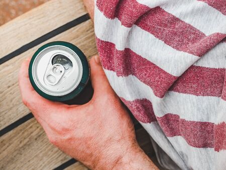 Can of beer, male hand on the background of a beautiful, wooden surface. Top view, close-up. Concept of leisure and travelの写真素材