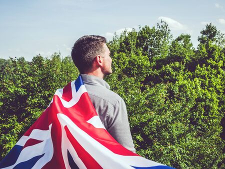 Attractive man holding British Flag on blue sky background on a clear, sunny day. View from the...