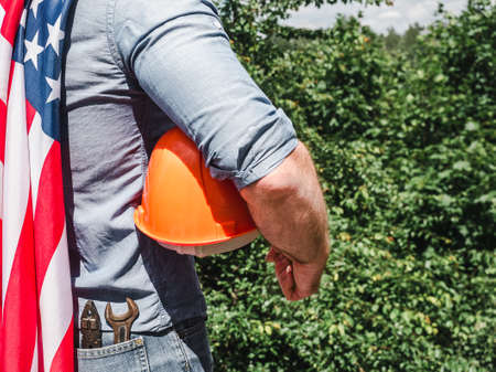 Handsome man with tools, holding an American Flag. View from the back, close-up. Concept of work and...