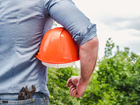 Attractive man with tools holding a safety helmet. View from the back, close-up. Concept of work and employmentの写真素材