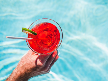 Beautiful glass with a refresh cocktail and an attractive man on the background of the swim pool. Top view, close-up. Vacation and travel concept. Moments of celebrationの写真素材