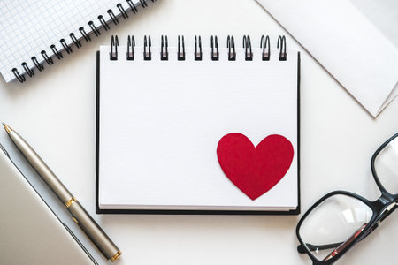 Blank notepad page and red heart drawing. Congratulatory inscriptions. Close-up, indoors. Studio...