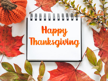 Happy Thanksgiving. Greeting card and congratulatory inscription. Bright pumpkin, tree leaves and colorful flowers lying on an empty table. Close-up, view from above. Holiday preparation conceptの写真素材