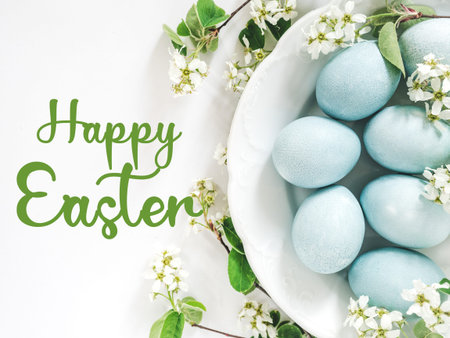 Happy Easter. Pastel blue Easter eggs on a white table with spring blossoms and a congratulatory...