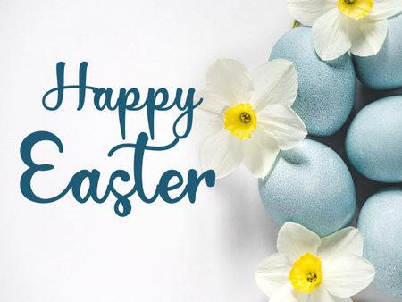 Happy Easter. Pastel blue Easter eggs on a white table with spring blossoms and a congratulatory...