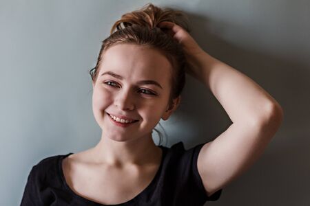 A young smiling girl adjusts her hair with her hand against the blue wallの写真素材