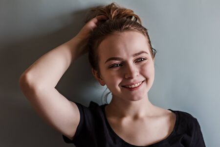 A young smiling girl adjusts her hair with her hand against the blue wallの写真素材