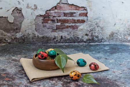Happy Easter, quail painted spotted eggs in a wooden bowl on a linen towel and green leaves, a...