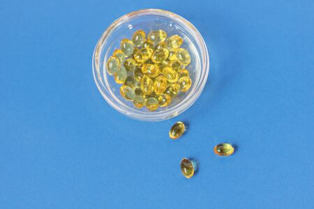 Yellow gelatin capsules with vitamin D3 in a glass container on a blue background. Pharmaceutical therapeutic and prophylactic preparation of vitamin D deficiency in adults and childrenの写真素材