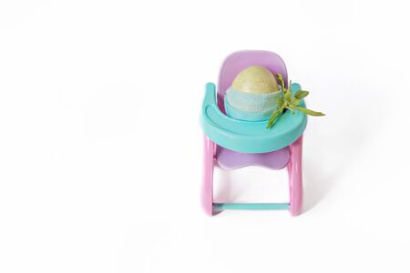 Easter egg in a protective mask sits in a highchair with a bouquet .Easter holiday during the coronavirus pandemic.The concept of protection Covid-19の写真素材