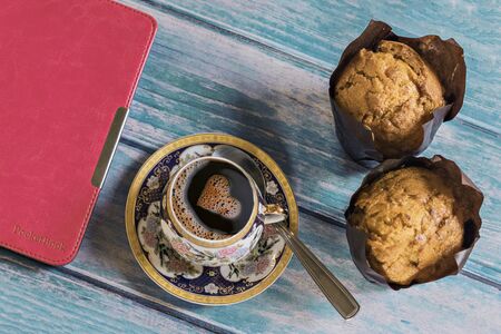 Vanilla cupcake and a cup of black coffee with heart-shaped foam, a pink cover tablet on a blue wooden table background.の写真素材