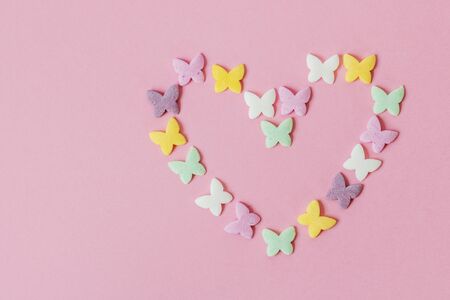 Pastry multicolored sprinkles-butterflies are laid out in the shape of a heart on a pink background. Decoration of confectionery productsの写真素材