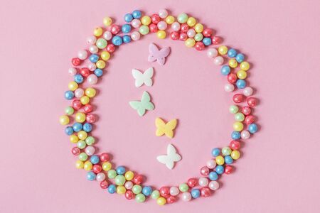 Pastry sprinkles are scattered in the form of a circle, inside it are enclosed colorful butterflies on a pink background.の写真素材
