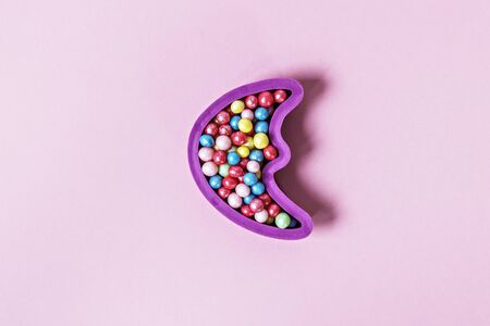 Pastry sprinkles in the form of multicolored balls in a mold in the form of a month moon on a pink background.の写真素材