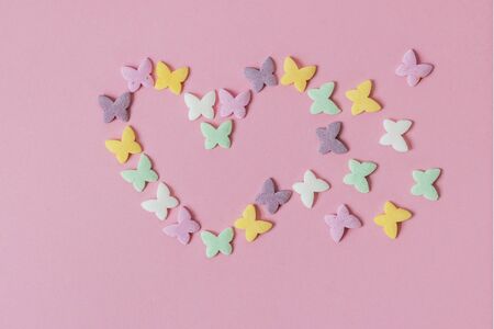 Pastry multicolored sprinkles-butterflies are laid out in the form of a decaying heart on a pink background. Decoration of confectionery productsの写真素材