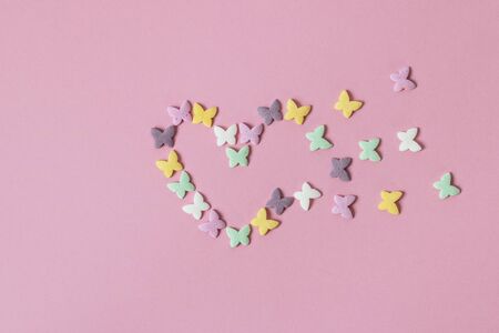 Pastry multicolored sprinkles-butterflies are laid out in the form of a decaying heart on a pink background. Decoration of confectionery productsの写真素材