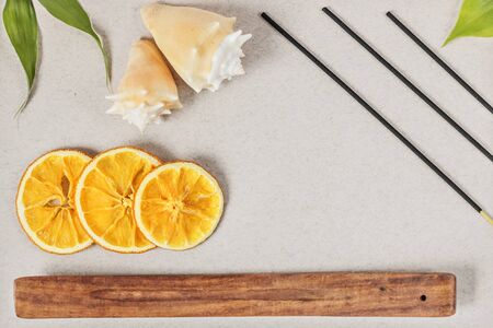 Incense sticks with a stand, sliced orange circles in a wooden bowl on a gray background. Also a seashell.Aromatherapy. The concept of home Spa.の写真素材
