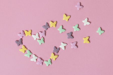 Pastry multicolored sprinkles-butterflies are laid out in the form of a decaying heart on a pink background. Decoration of confectionery productsの写真素材