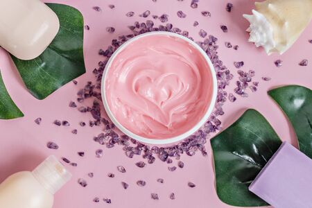 Natural organic cosmetics: body cream, bath salt, lavender and peach soap, shower gel, seashell with monstera leaves on a pink background. Flat lay.The concept of skin care and beauty. Spa home.の写真素材