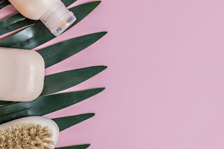 On a pink background with green leaves, a body brush, peach soap and shower gel. Body care. Spa home conceptの写真素材