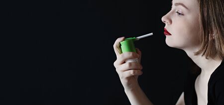 A young woman using a painkiller with an antiseptic spray to soften her throat, remove the pain.Glossy oral spray or aerosol bottle for the prevention and treatment of respiratory infections.の写真素材