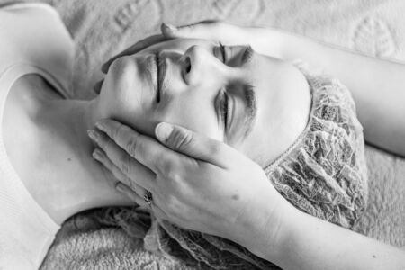 A young woman gets a relaxing facial massage. Facial skin care. Beauty and spa concept. Black and whiteの写真素材