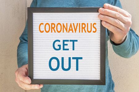 A man holds a placard with the text message "CORONAVIRUS GET OUT". The end of quarantine. Hotel, cafe, local store, service owner meets guests after the coronavirus pandemic and isolation of peopleの写真素材