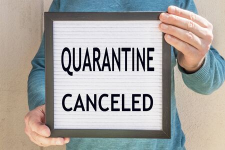 A man holds a placard with the text message QUARANTINE CANCELED . The end of quarantine. Hotel, cafe, local store, service owner meets guests after the coronavirus pandemic and isolation of peopleの写真素材