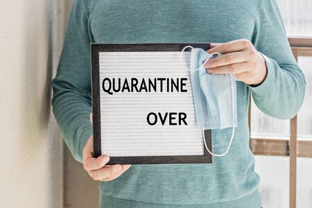 A man holds a placard with the text message "QUARANTINE OVER".The end of quarantine. Hotel, cafe, local store, service owner meets guests after the coronavirus pandemic and isolation of peopleの写真素材
