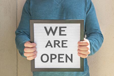 A man holds a placard with the welcome text message We are open . The end of quarantine. Hotel, cafe, local store, service owner meets guests after the coronavirus pandemic and isolation of peopleの写真素材