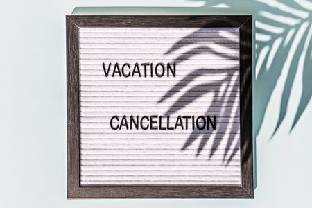 A message Board with the words vacation cancellation on a blue background. On the Board, the shadow of a palm leaf. Concept pandemic coronavirus and the global crisisの写真素材