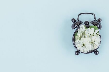 Spring and summer time from cherry flowers and a clock on a blue background. Flat lay, top view. Banner.の写真素材