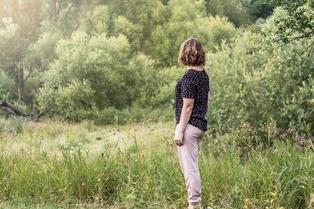 A young woman stands with her back to the forest. Summertime.の写真素材