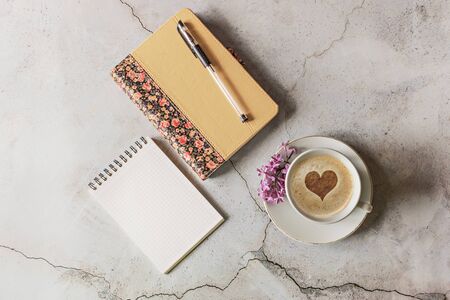 On the table with notebooks, a pen for writing is a Cup of cappuccino and foam in the form of a heartの写真素材