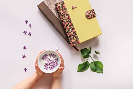In children's hands, a Cup of milk and lilac flowers. Books and leaves with lilac flowers are spread out on the table.の写真素材