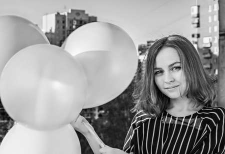 Young girl with balloons on the balcony of the apartment. Birthday. Black and white.