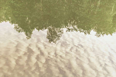 Reflection of trees and sky with clouds in lake water at sunset.
