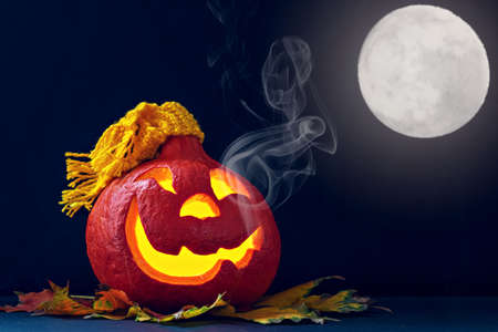 Glowing pumpkin in a hat with smoke and autumn leaves on a dark background. Jack's Lantern. Halloween Decorations.の写真素材