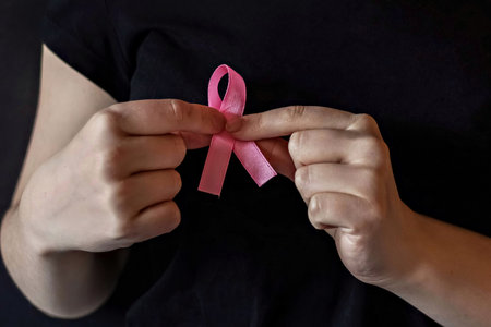 A girl in a black t-shirt with a pink ribbon on her chest is fighting cancer. Breast cancer awareness month. The concept of breast cancerの写真素材