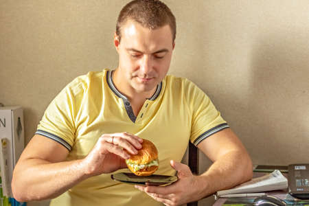 Young hungry man eating a burger. The guy eats fast food, unhealthy food. Diet conceptの写真素材
