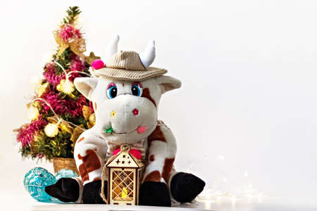White soft toy bull on a light background with a Christmas tree and garlands, New Year's card. Chinese Year of the Ox, zodiac symbol 2021.の写真素材