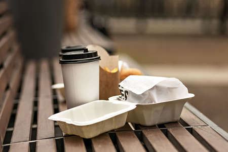 Fast food. Paper cups with coffee, hamburger boxes and fries on a park bench. Takeaway food concept.の写真素材