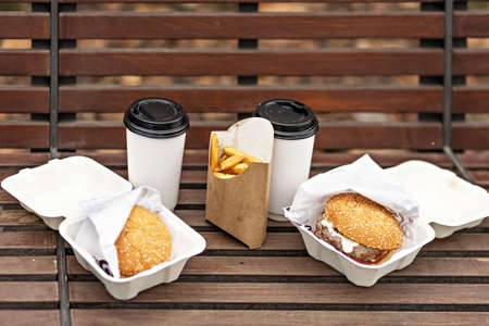 Young woman working on laptop sitting on a park bench with coffee. Computer and online shopping use. Distance learning, online educationの写真素材
